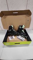 Pair of black and light green ladies roller blades inside open original box on table.