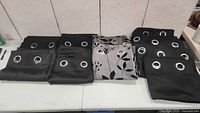 Curtain panels folded on a table showing metal grommets and the mix of black and patterned curtains.