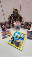 Wide shot showing all toys in lot including Bumblebee Transformer, Marvel Black Widow figure, boxed toys, and book.