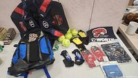 Image showing multiple sports bags including a black and blue backpack and two black and red sports bags with softball logos. Also shows yellow softballs, yellow and black gloves, blue protective pads, and a black Adidas bag.