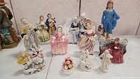 Group of 12 porcelain collectible figurines arranged on a surface, showing Victorian era styled characters in various poses and outfits.