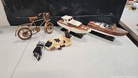 Overview of all items in lot showing metal bicycle, two wooden boats on stands, and ceramic cow with coiled wire accessory