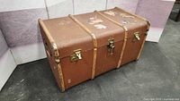 Full view of the closed vintage steamer trunk showing brown exterior, metal locks, and reinforcements.