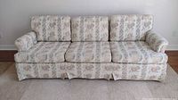 Front view of a floral patterned 3 seat sofa with cushions and pleated skirt, showing the upholstery and condition.