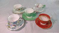 Five assorted bone china teacups with matching saucers displayed on white background, showing various floral patterns and color schemes.