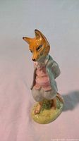 Front view of the fox figurine standing upright, showing detailed coloration and clothing.