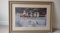 Front view of the framed print titled 'Bottoms Up' showing seven children on a fence in an outdoor setting. The frame is wide and textured with a matte border.