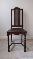 Front view of the vintage cane back chair showing carved top, cane weave backrest, and barley twist legs.