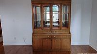 Front view of full wood china cabinet with glass doors and lower storage cabinets on hardwood floor