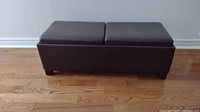 Front view of the closed coffee table/footrest in dark brown faux leather with split padded top.