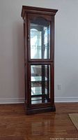 Full view of the curio cabinet showing the two glass front doors, walnut wood frame, and brass handle.