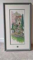 Front view of framed artwork showing the print of a hillside cottage with plants and flowers, signed and numbered.