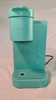 Front view of turquoise Keurig K-Express Essentials coffee maker showing water reservoir, control buttons, and drip tray.