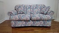 Front view of the floral loveseat with matching throw pillows placed on each end, showing the full piece including wooden feet.