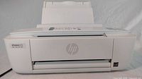 Closed front view of the white HP Deskjet 3700 printer with paper loaded in the top feeder tray.
