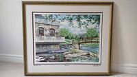 Framed artwork on wall showing print with river scene and stone building, signed and numbered 65/550.