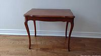 Front view of wooden side table showing curved legs and scalloped edges on tabletop with surface wear visible.