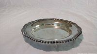 Side view of the silver plated butter dish tray showing its depth and ornate beaded scalloped edge.