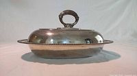 Closed silver plated serving dish with domed lid and handle, photographed from the side on a neutral background.