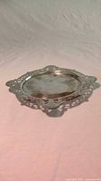 Angled side view showing overall form and decorative pierced edge of the silver plated tray on a light fabric background.