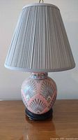 Full view of table lamp showing gray pleated fabric shade and scalloped ceramic base on wooden stand.