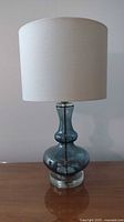 Full view of blue glass table lamp with linen shade, showing height and overall design.
