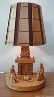 Full view of the wooden table lamp showing lampshade and base with fireplace and wooden figurines
