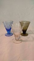 Front angle view of three vintage shot glasses in blue, pink, and green glass with etched star patterns.