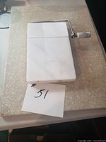 Marble cheese slicer resting on larger stone cutting board with lot number card