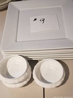 Stack of six white square plates with two of the scalloped bowls in front