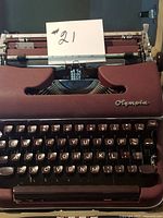Front view of burgundy Olympia Deluxe typewriter showing keyboard and branding