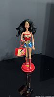 Full view of Barbie as Wonder Woman on red stand holding lasso and lunchbox