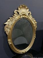 Front view of gold ornate oval mirror with shell and floral frame