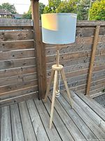 Full view of IKEA LAUTERS tripod floor lamp with white shade on wood deck background