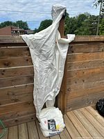 White disposable coverall hanging on railing with packaged shoe covers at base