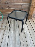 Full view of black metal outdoor side table with glass top on deck