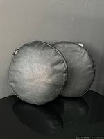 Front view of both black round pillows showing faux leather texture