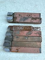 Seven steel lathe tool bits laid out, carbide tips visible