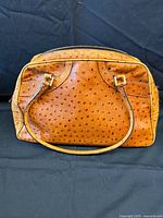 Front view of tan faux ostrich leather handbag with dual top handles