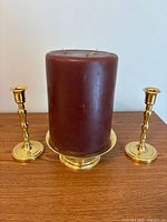 Front view of brass candlesticks flanking pedestal platter with burgundy candle
