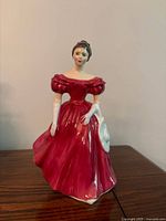 Front view of Royal Doulton figurine in red dress holding white hat