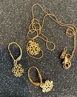 Pendant on chain and both earrings displayed on dark glitter surface