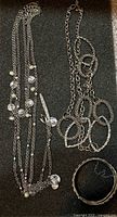 All three jewelry pieces laid flat: multi-strand necklace, oval link chain necklace, braided bangle
