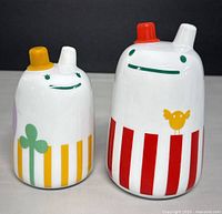 Front view of both containers showing smiling faces, spouts, and colorful vertical stripes and motifs.