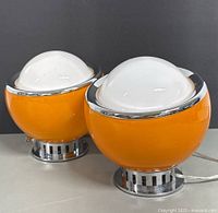 Front and angled side view of the two orange and white glass modernist table lamps next to each other on a flat surface.