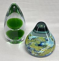 Two hand blown art glass paperweights shown side by side on a white surface, clear view of both items