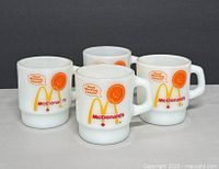 Four vintage Fire King mugs arranged with logos visible, showing McDonald's Canada design featuring a cheerful sun graphic and 'Good Morning Canada!' text in orange, with a small Canadian maple leaf.
