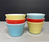 Front angled view of six stacked vintage Pyrex small bowls in yellow, red, and blue colors.
