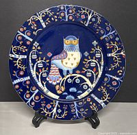 Front view of the blue ceramic platter with owl and tree design on a black stand.