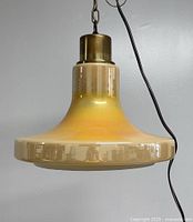 Front view of the pendant light showing the wide cased glass shade with a yellow-orange luster finish and brass-tone upper fitting with hanging chain and cord.